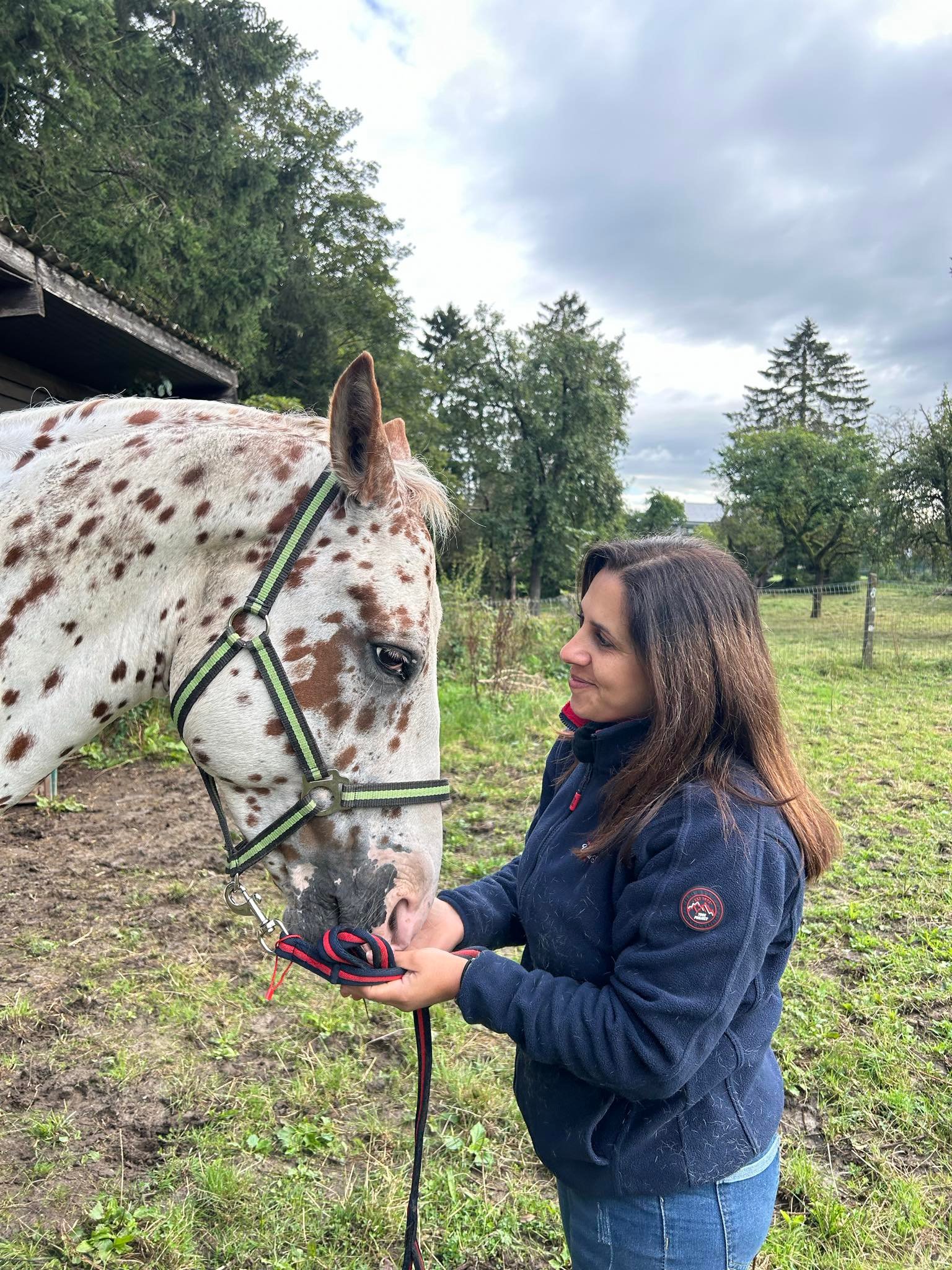 Laura Fontana se tenant a la droite d'un cheval blanc a taches brune